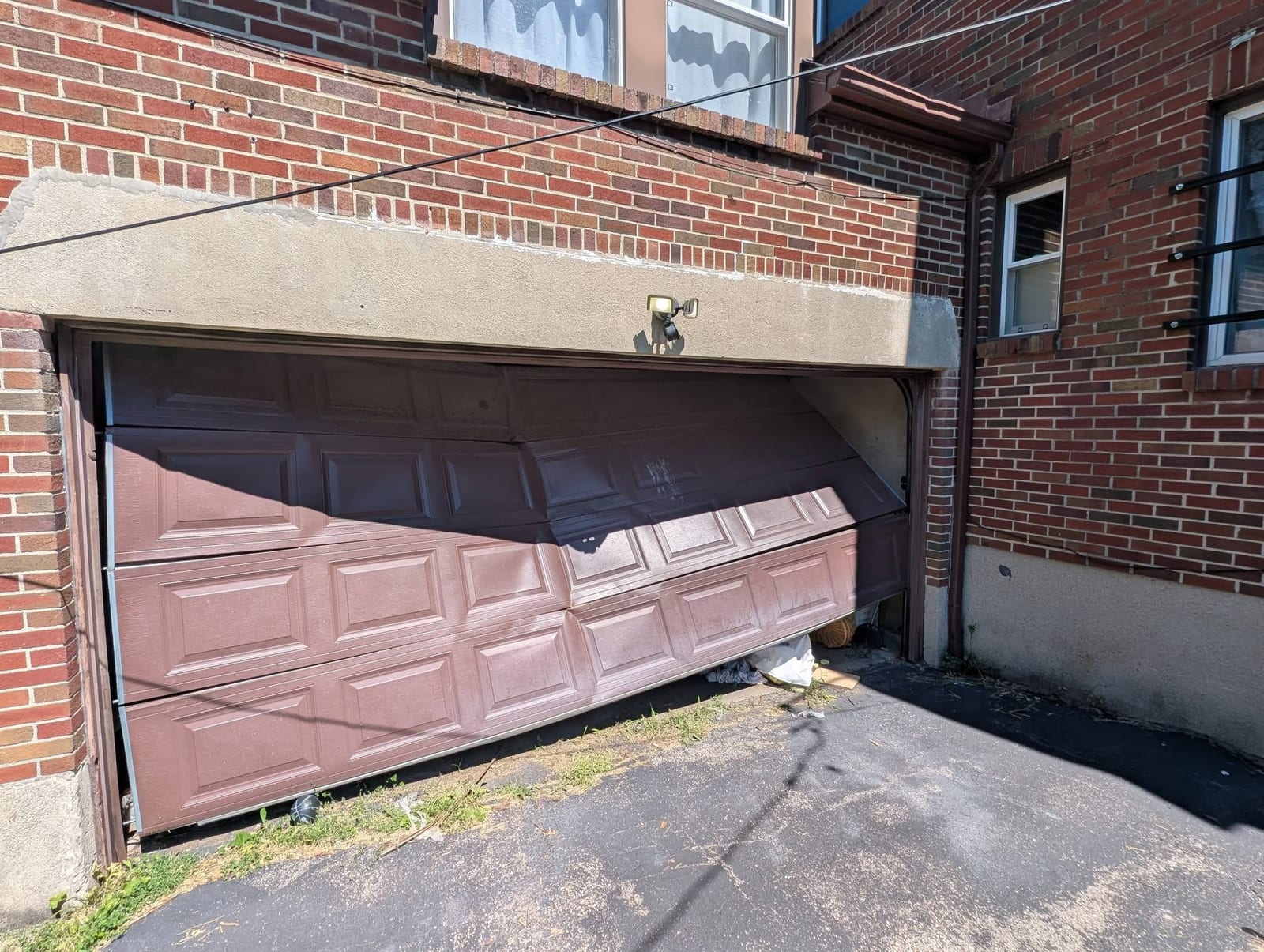 Severely buckled brown garage door on a brick home